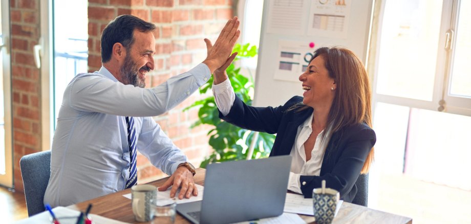 2 Menschen am Schreibtisch geben sich high five